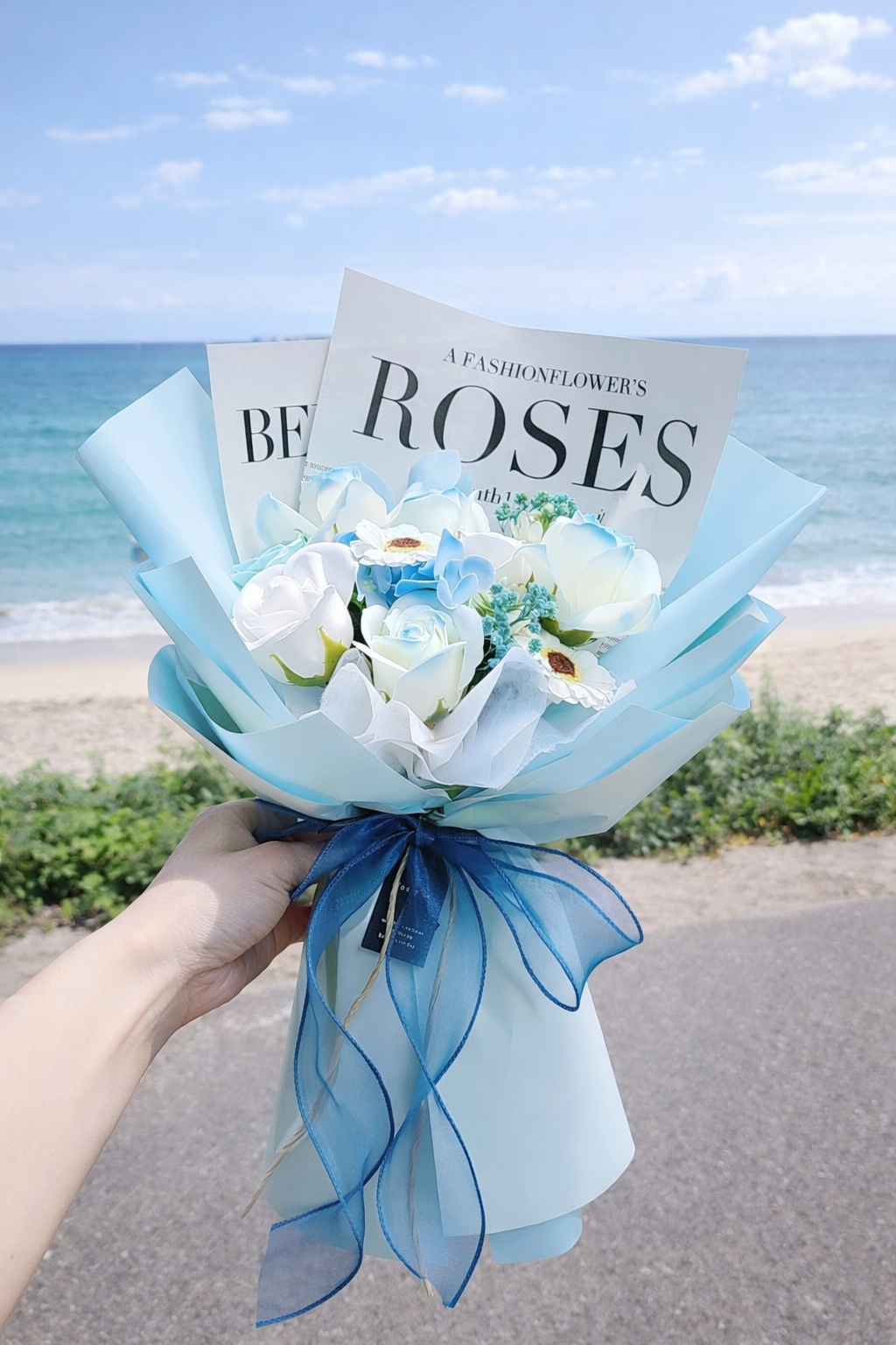 海辺で手に持たれたブルー系のアーティフィシャルフラワーブーケ